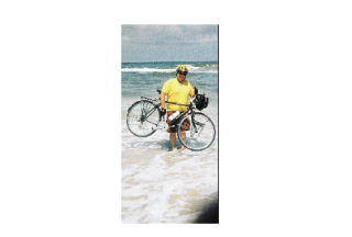 Rob Putnam holds his bike the in shallow waves of the Atlantic Ocean. This spring