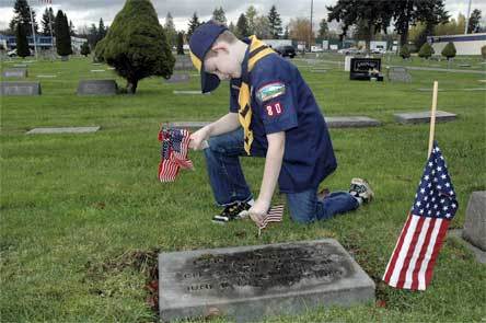 Marysville Cub Scout Tyler Killham places a flag near the headstone of a veteran on Nov. 11.