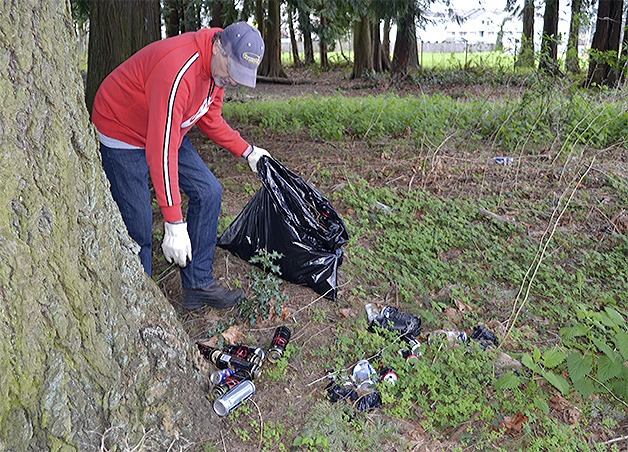 Ed Lozeau picks up beer cans littered in the trees near Marshall Elementary School in North Marysville. Despite the city's best efforts to keep them away