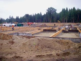 Workers prepare foundations for the Marysville Arts & Technology School on the new shared options campus.  Modular components built up the road at the Williams Scotsman factory in Smokey Point were trucked to the site and will be placed on the foundations by cranes.