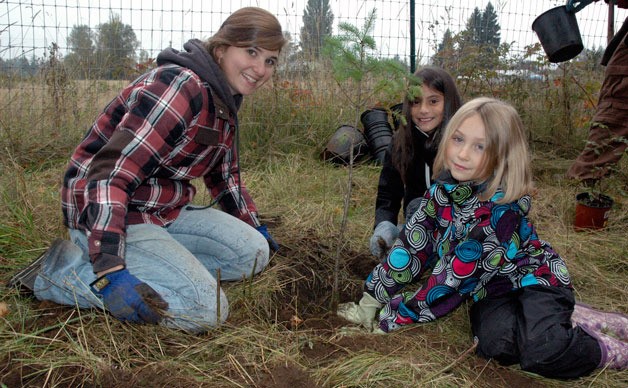 Grace Academy National Honor Society student Piper Wright helps Marshall Elementary third-graders Reya Moore and Savannah Buse plant trees near the banks of Allen Creek on Oct. 16.