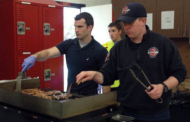 Fire academy applicant Mike Meehan and firefighter Brendan Magee prepare sausages at Getchell Fire Station 68 on April 20