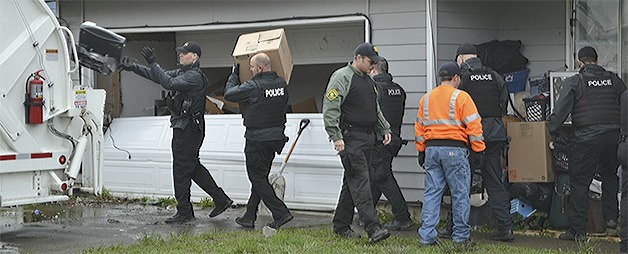 Police help city sanitation workers throw garbage into a truck prior to the house being boarded up for health reasons.