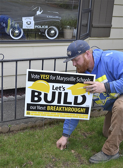 Aaron Stenson puts up a sign in his yard at his Marysville home. Even though he has no kids in the school system