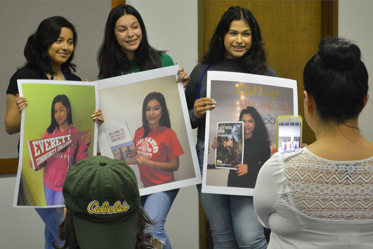 3 AVID students pose for family photos holding posters with pictures of themselves and flags of where they are going to college. (Steve Powell/Staff Photo)