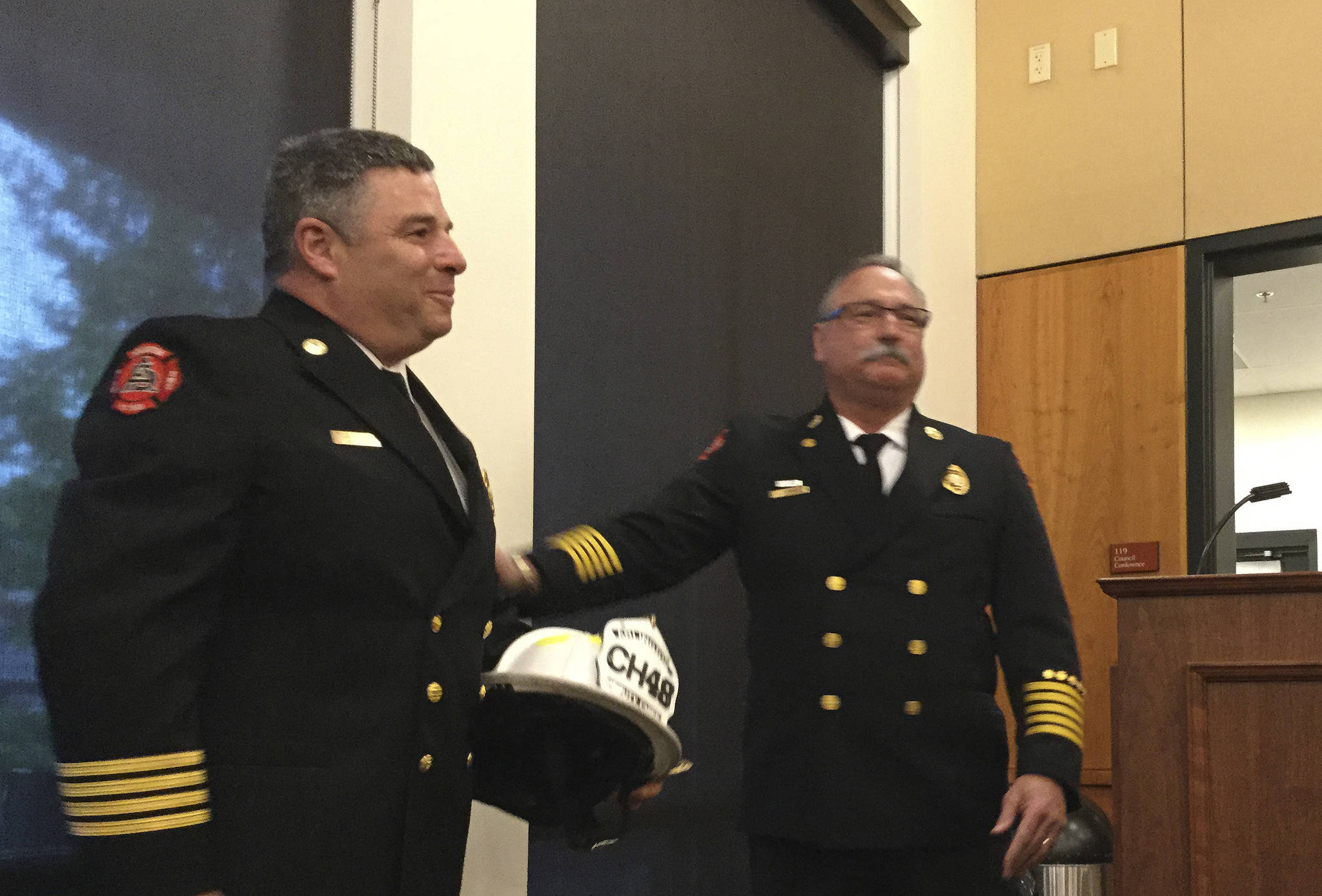 Arlington Chief Bruce Stedman presents Deputy Fire Chief Tom Cooper with his fire helmet and badge at a city council meeting. Cooper retired after 32 years.