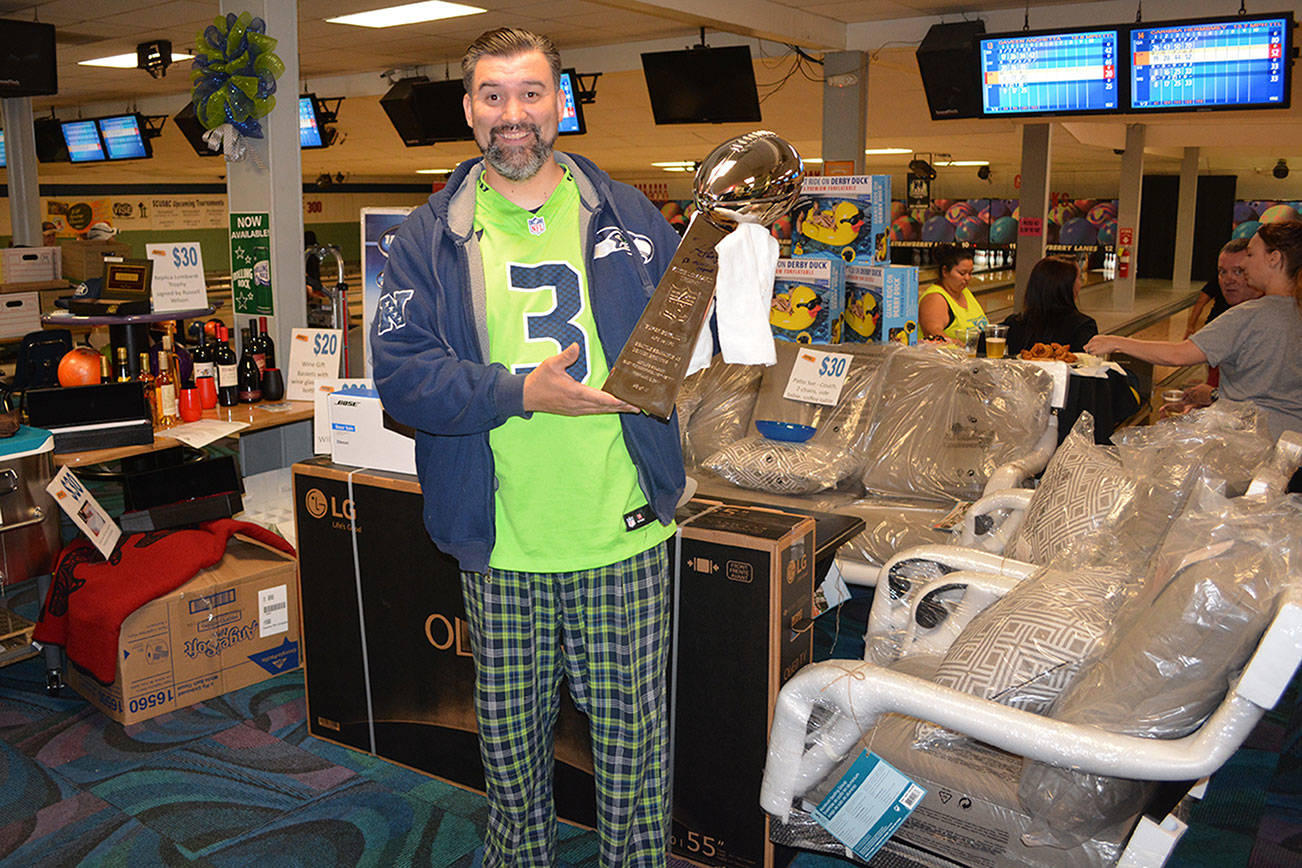 Shane Warbus, surrounded by other prizes, holds a Lombardi Trophy, one of the raffle gifts at the fundraiser for Junior Achievement. (Steve Powell/Staff Photo)
