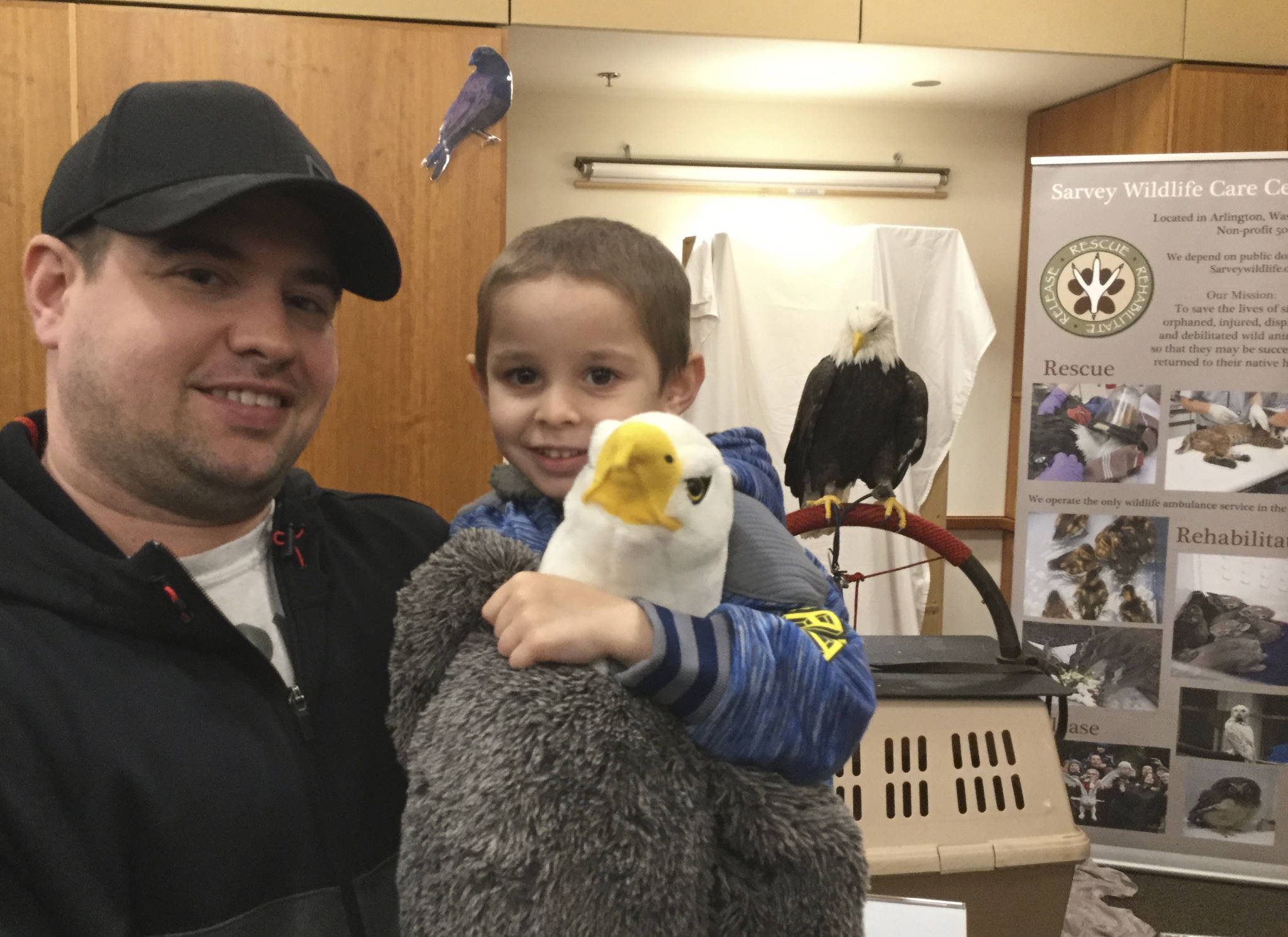 Robbie Turrone of Arlington, pictured with dad Robert, clutches his stuffed eagle toy while a real bald eagle, Freedom, looks on from behind. Freedom was the main attraction at a Sarvey Wildlife Center open house during last weekends annual Arlington Eagle Festival.