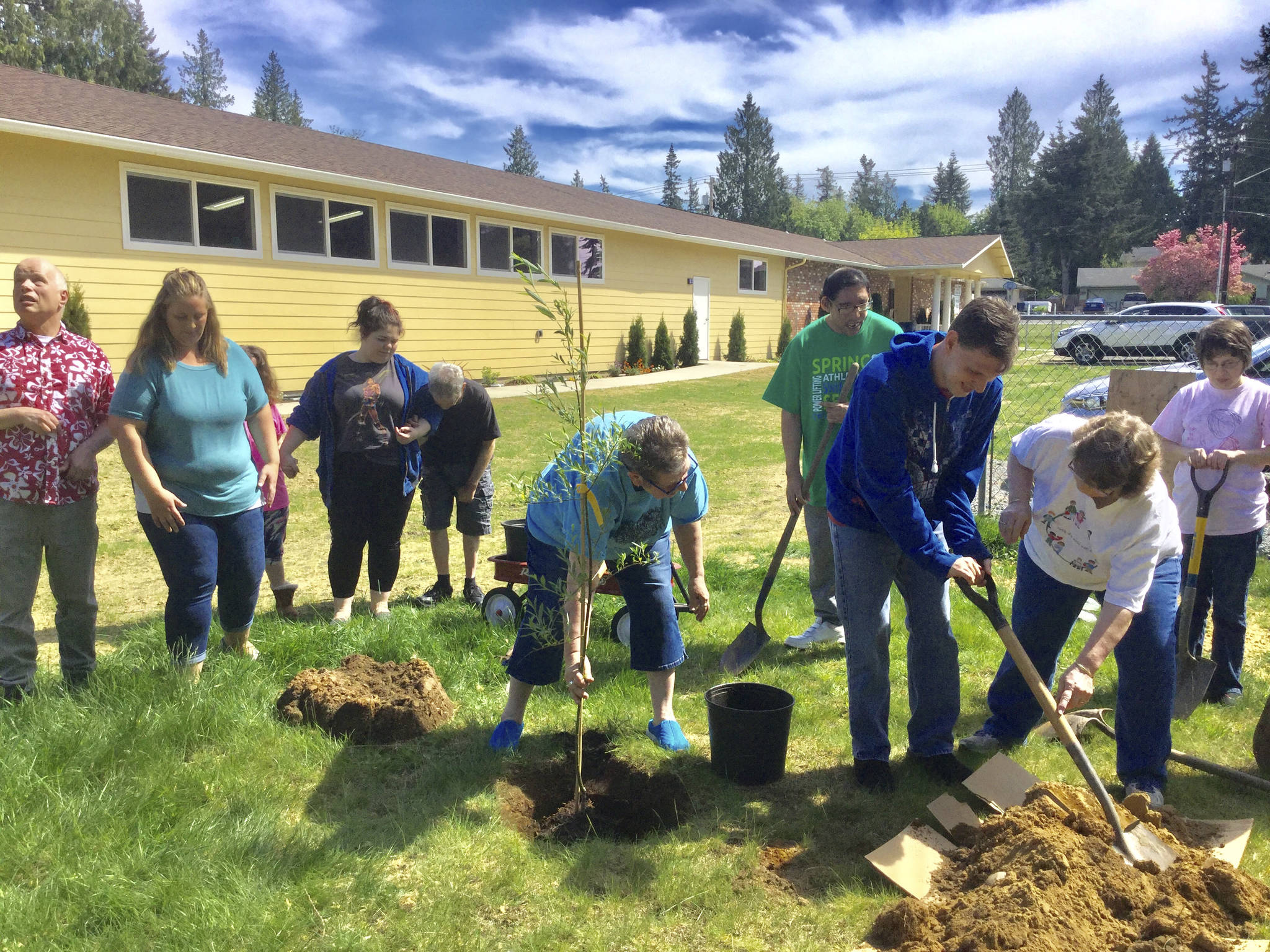 With help from Karen Harper, right, client Ray Molstad scoops a shovel of dirt to help caregiver Sue Williss plant a weeping willow in memory of her mother outside the newly-expanded Willow Place in Marysville, while other clients and staff from the recreation center for disabled adults wait their turn to help.