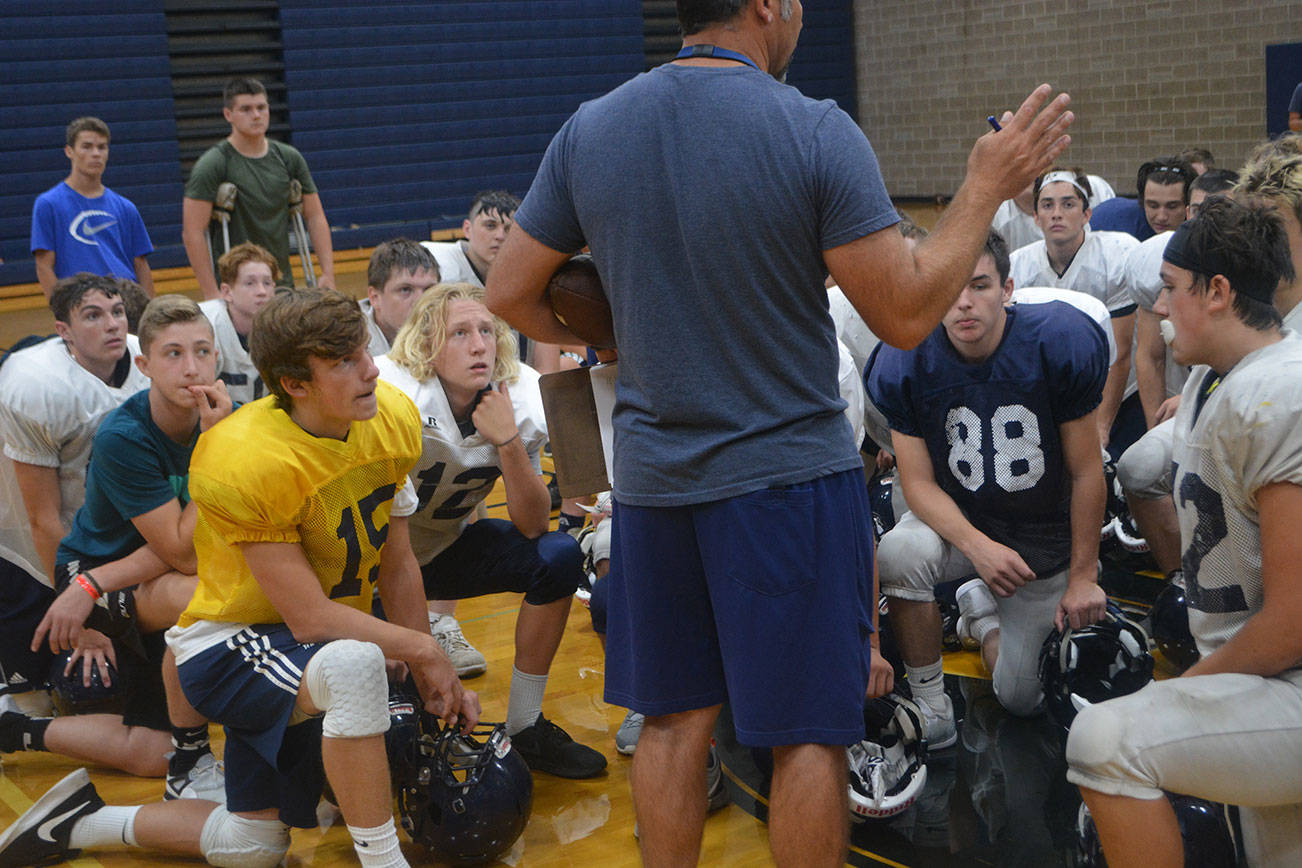 Anthony Whitis, in yellow, listens with his team to Eagle coach Greg Dailer at practice earlier this season. Whitis, a senior, led Arlington to a come-from-behind win over Ferndale Friday night.