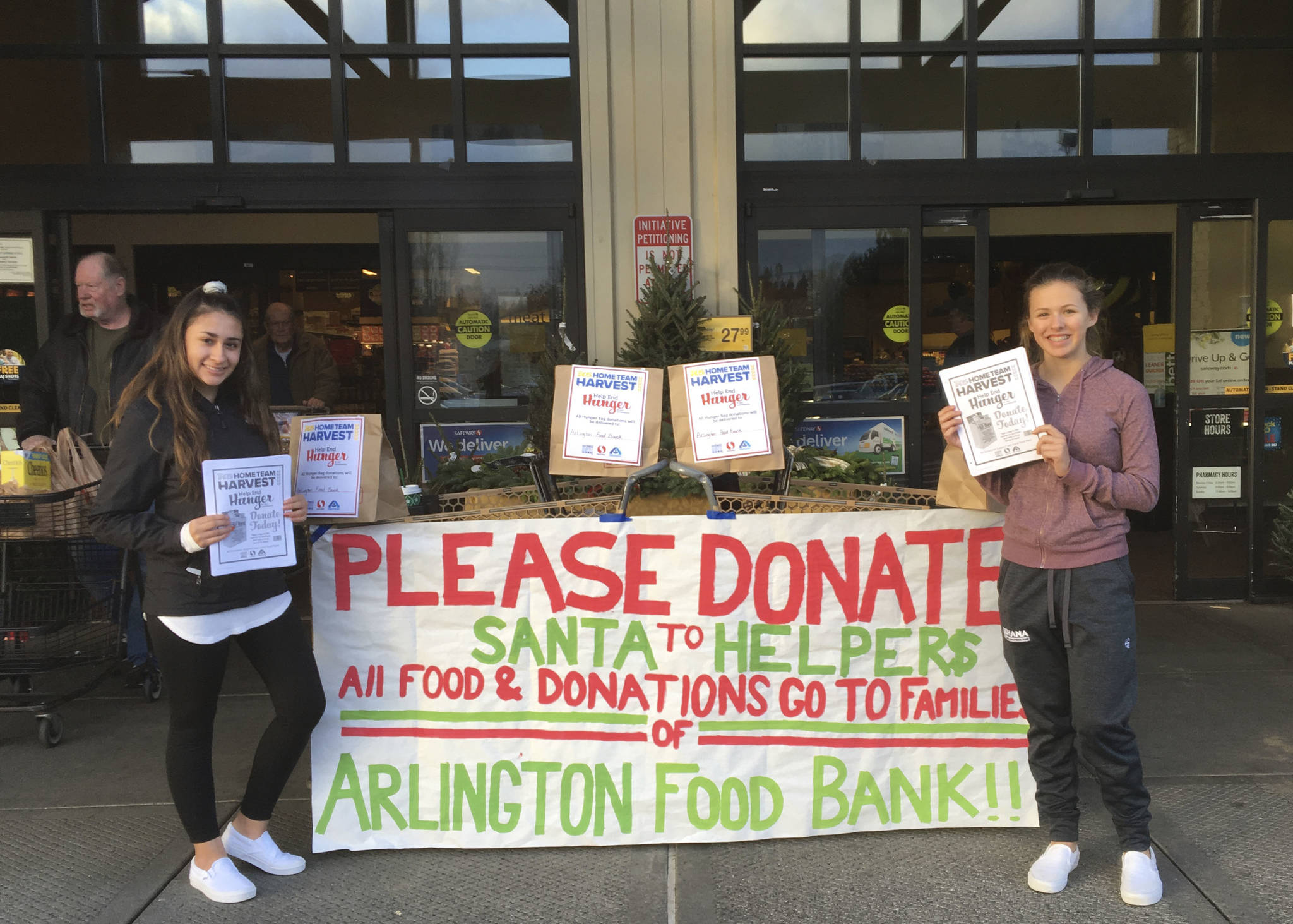 Arlington High School DECA students Amari Garrissey (left) and Amelia Hale are Santa’s Helpers volunteering outside the Arlington Safeway store to collect food, toys and donations for families in need during the holidays.