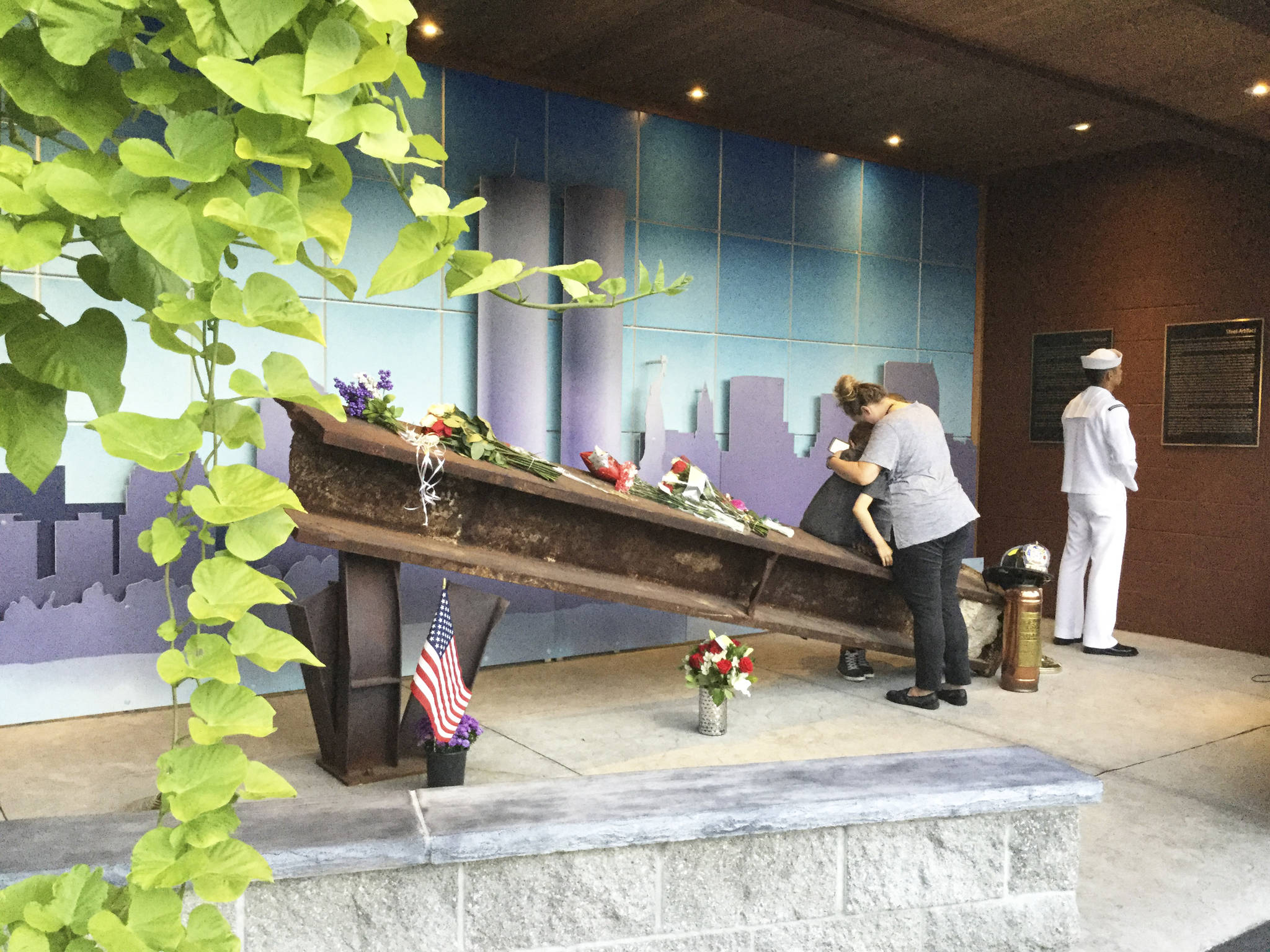 A family hugs at Station No. 46s Arlington Remembers Memorial where a 13-foot, 4,373-pound steel beam from the destroyed World Trade Center towers now rests, while a sailor reads the story behind how firefighters drove cross-country to bring the steel artifact to Arlington.