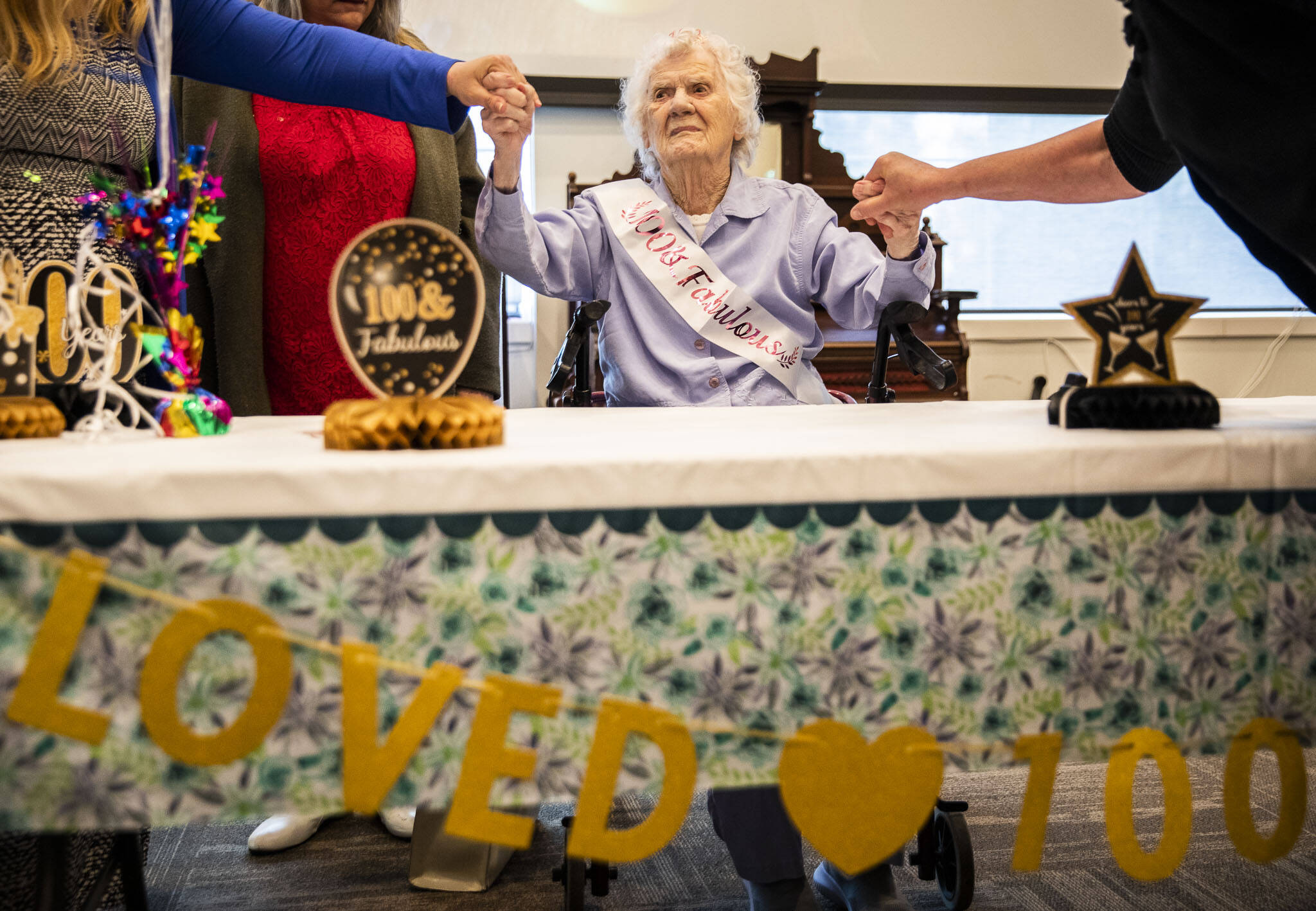 From her seat of honor, Ferne Ullestad holds family members’ hands during her 100th birthday celebration April 30. (Olivia Vanni / The Herald)