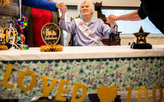 Ferne Violet Berg Ullestad holds hands of her family members while she sits are her table during her 100 year birthday celebration on Saturday, April 30, 2022 in Marysville, Washington. (Olivia Vanni / The Herald)